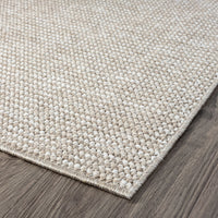 Taupe flatweave rug with subtle textured geometric pattern on dark wood floor.