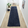 Navy blue modern shaggy runner rug on light wood floor in narrow hallway.