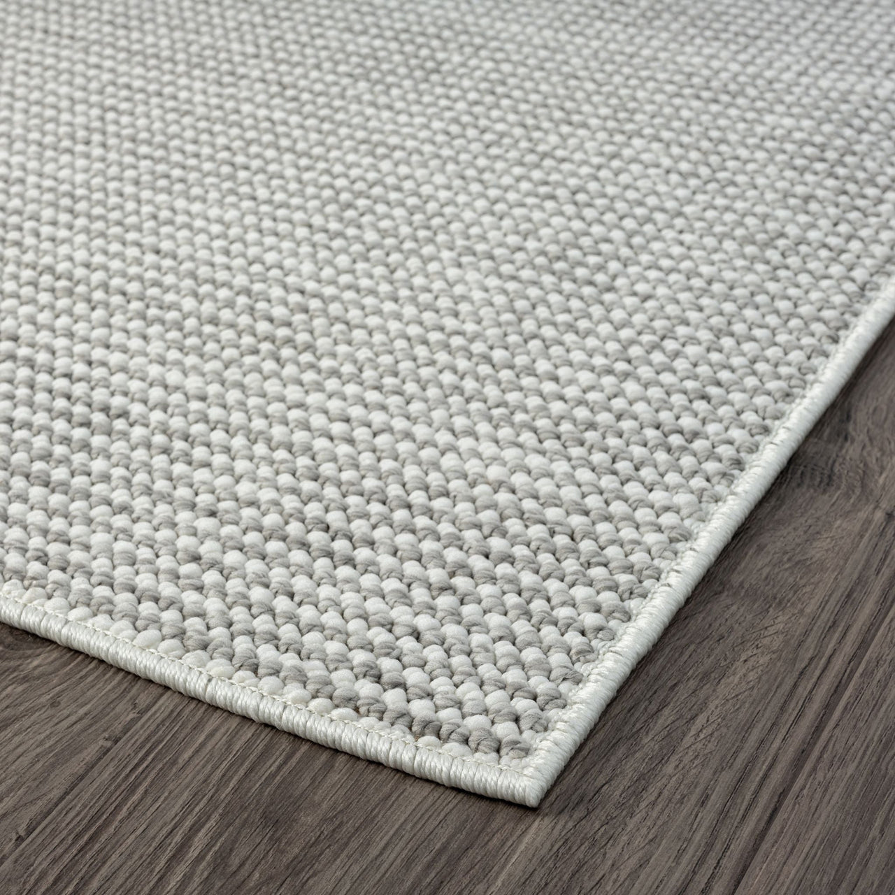 Close-up of a silver grey flatweave rug corner with a subtle textured pattern on dark wood floor.