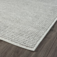 Close-up of a silver grey flatweave rug corner with a subtle textured pattern on dark wood floor.
