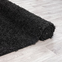 Black shaggy rug with thick polyester fibers, partially rolled on light wood floor.