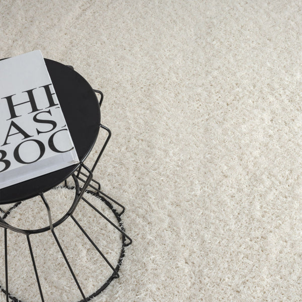 Cream-colored modern shaggy rug with plush polyester fibers and soft texture next to a black wire side table.