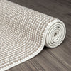 Rolled beige and cream flatweave runner rug with textured geometric pattern on wood floor.