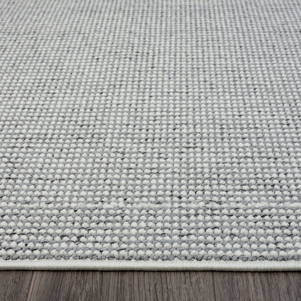 Grey flatweave rug with subtle textured geometric pattern and white edge trim on wooden floor.