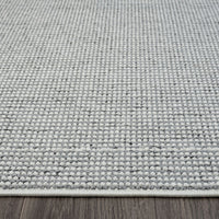 Grey flatweave rug with subtle textured geometric pattern and white edge trim on wooden floor.