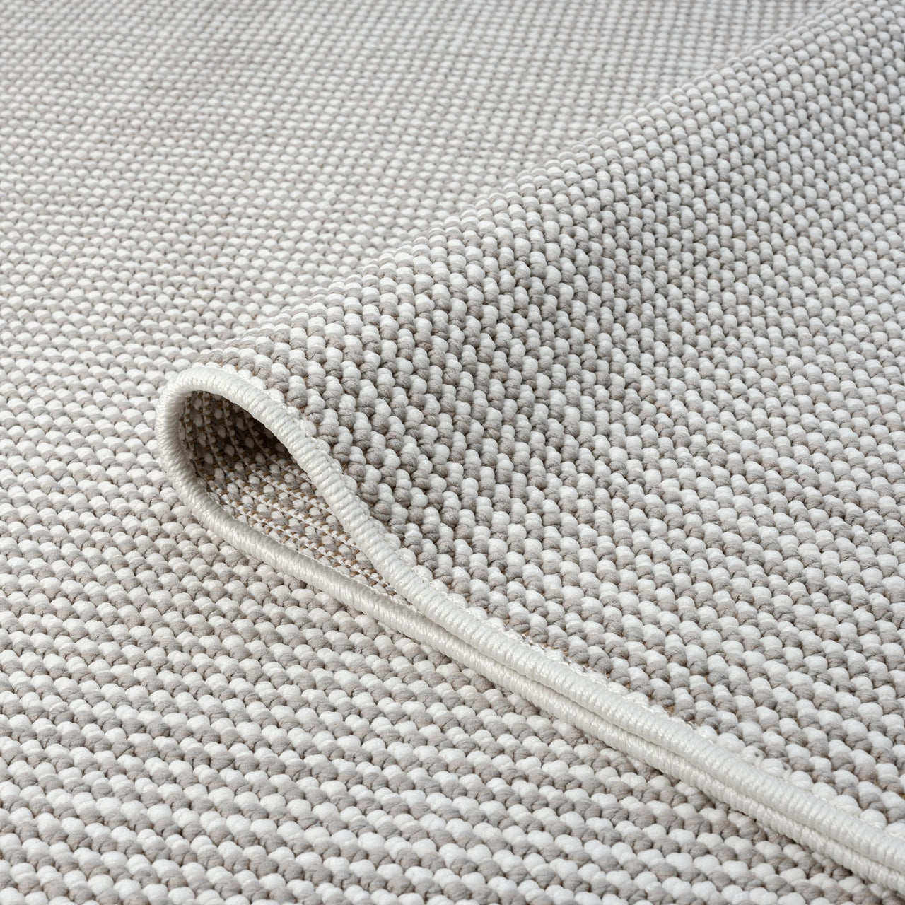 Close-up of grey flatweave rug with tightly woven textured geometric pattern and neatly finished edge.