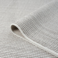 Close-up of grey flatweave rug with tightly woven textured geometric pattern and neatly finished edge.