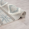 Rolled grey and beige geometric patterned runner rug with textured fringed edges on light wood floor.