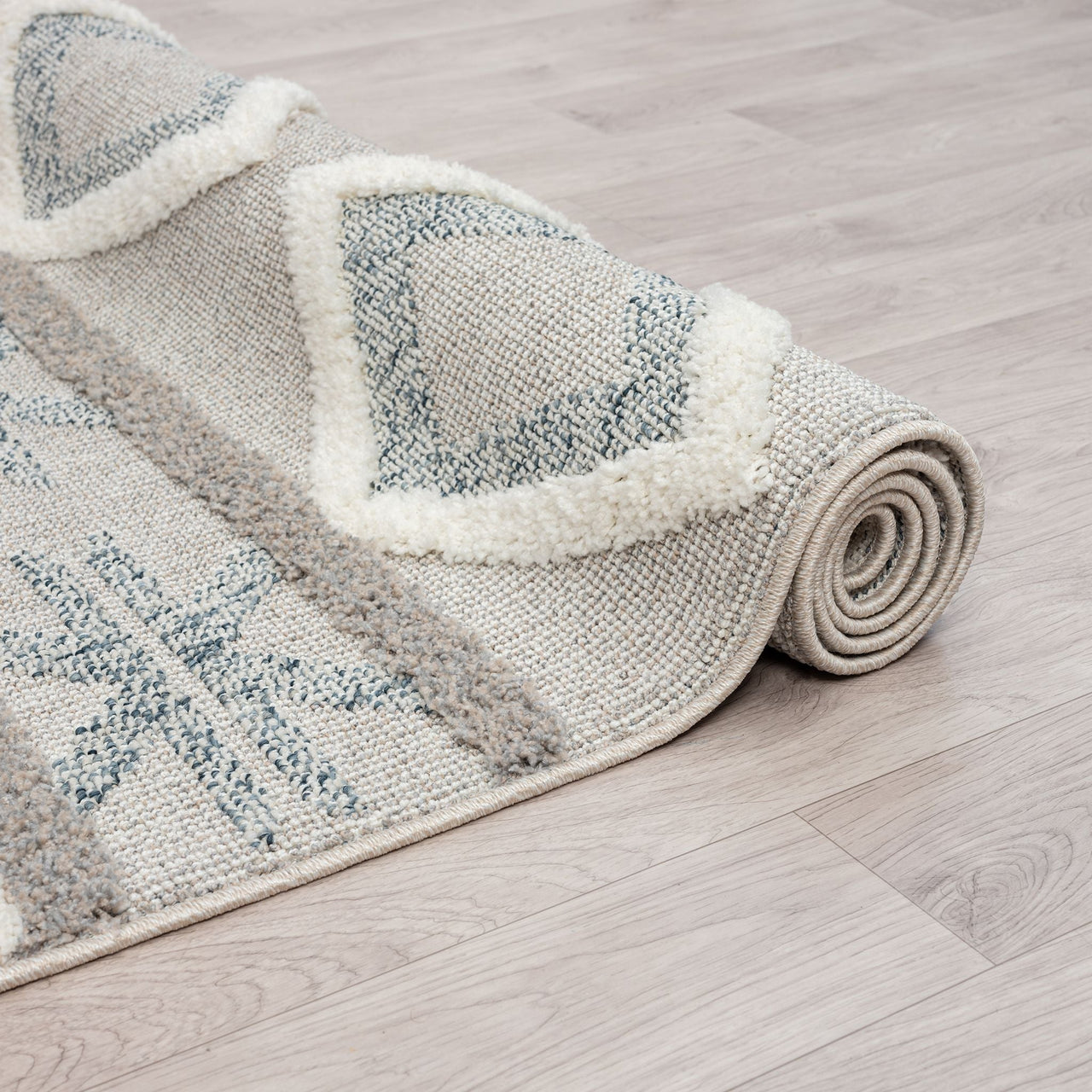 Rolled grey and beige geometric patterned runner rug with textured fringed edges on light wood floor.