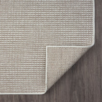Beige flatweave rug with subtle geometric pattern and neatly finished edges on dark wood floor.
