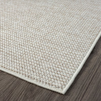 Beige flatweave rug with tight geometric pattern and clean, finished edges on wood floor.