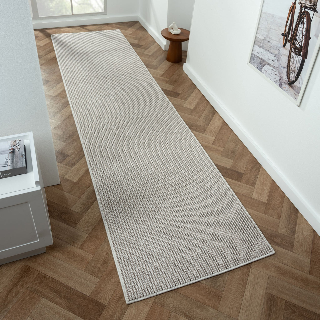 Beige flatweave runner rug with subtle geometric pattern on herringbone wood floor.