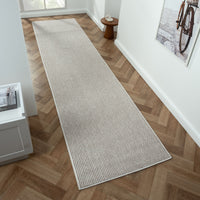 Beige flatweave runner rug with subtle geometric pattern on herringbone wood floor.