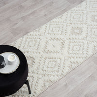Beige and white runner rug with textured geometric diamond pattern and fringed edges on light wood floor.