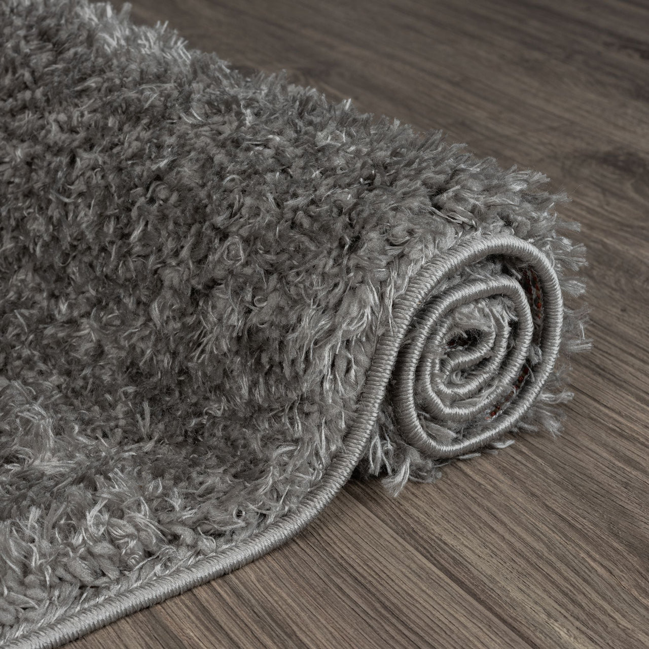 Rolled grey shaggy rug with thick polyester fibers on wooden floor, modern style.