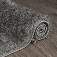 Rolled grey shaggy rug with thick polyester fibers on wooden floor, modern style.