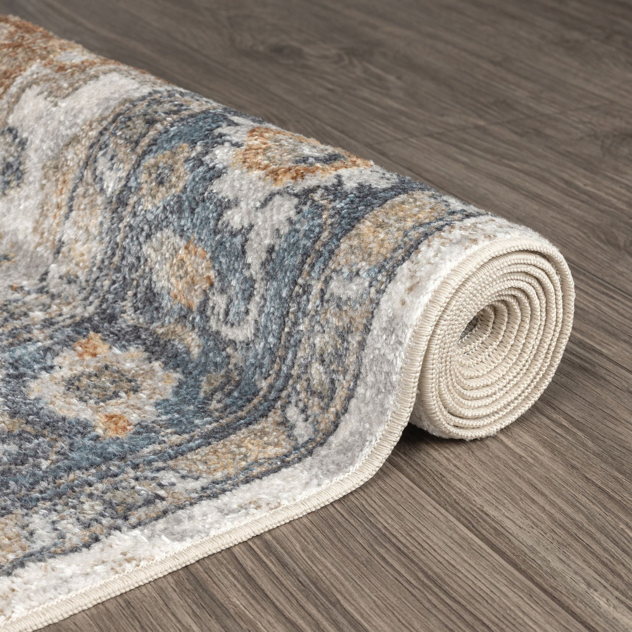 Rolled runner rug with blue, beige, and gray floral pattern on wooden floor.