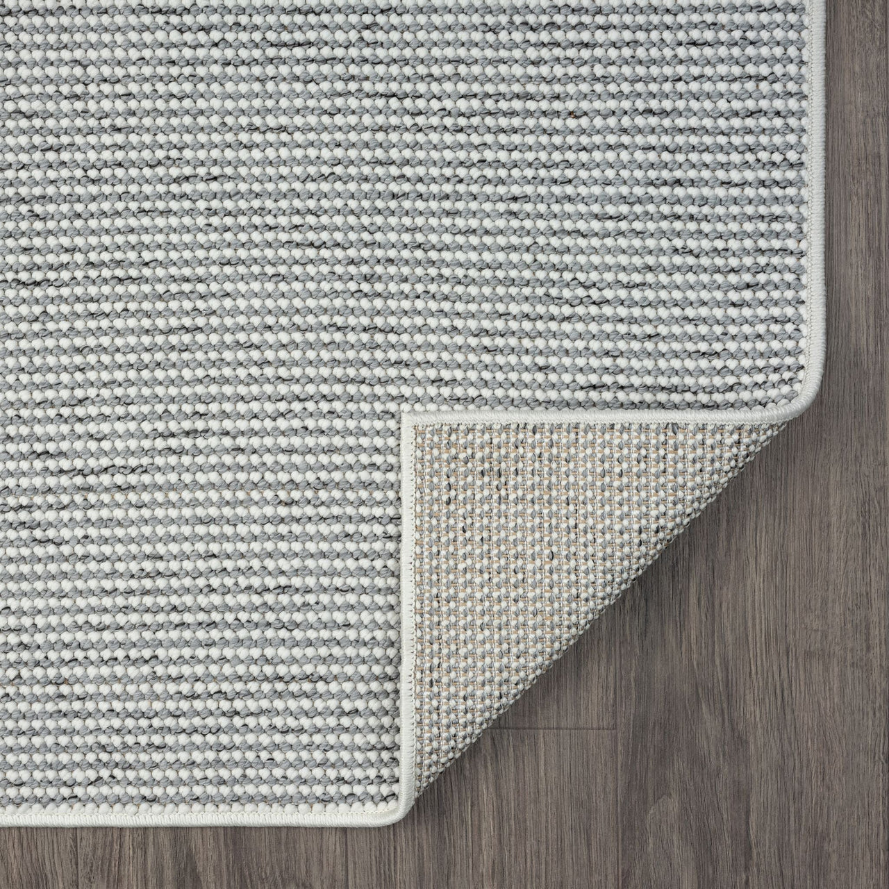 Grey flatweave rug with subtle geometric texture and clean stitched edges on wood floor.
