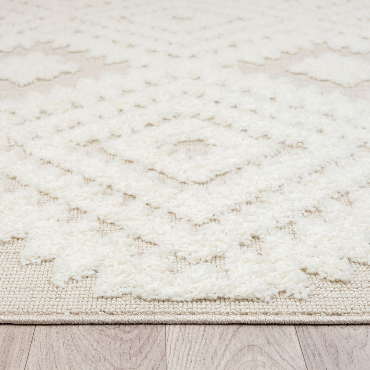 Beige and white Ceduna 2255 rug with textured geometric diamond pattern and fringe edges on wood floor.