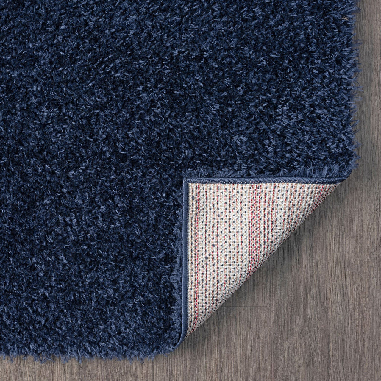 Navy blue modern shaggy runner rug corner showing dense polyester fibers and textured backing on wood floor.
