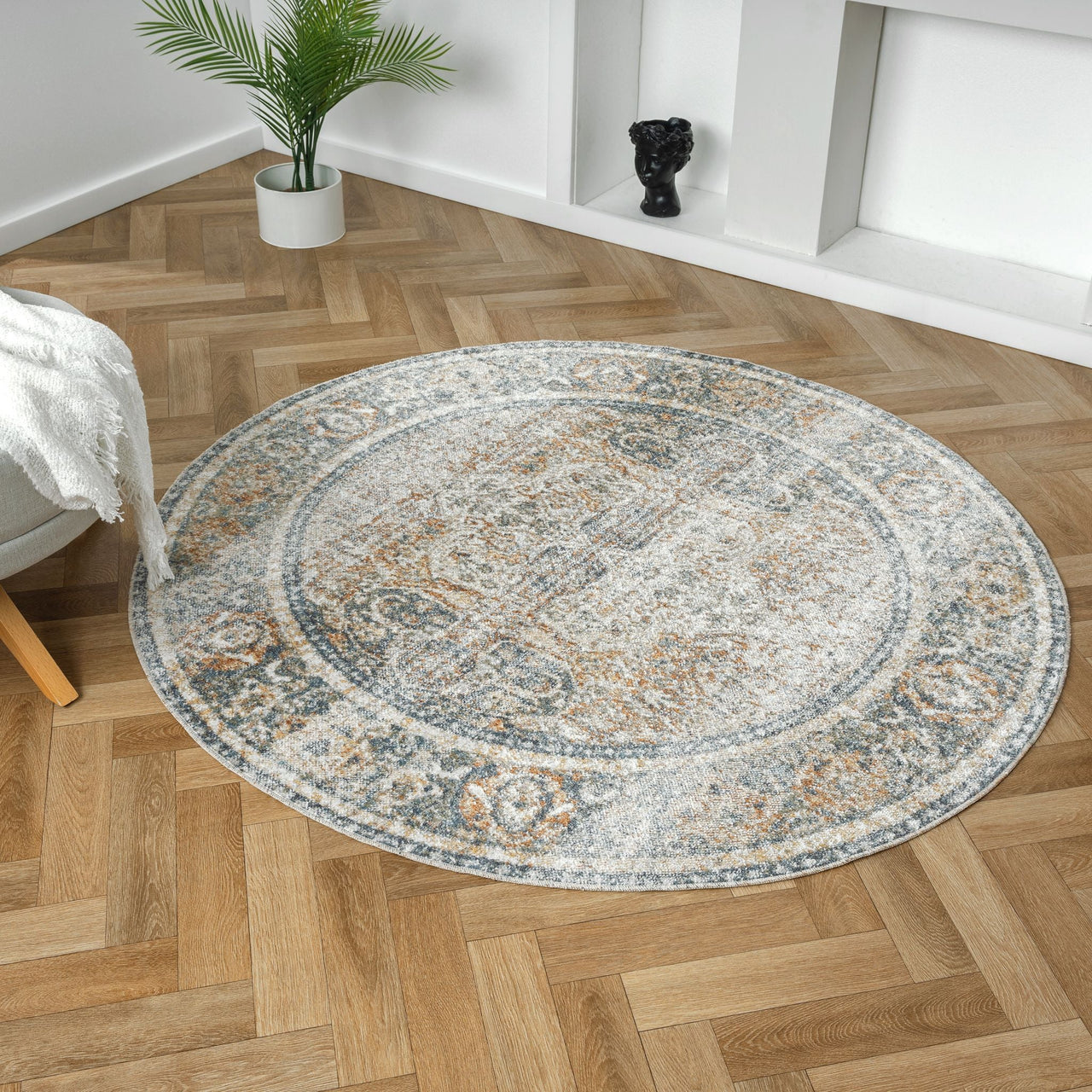 Round coral and gray vintage-style rug with intricate medallion pattern on wooden parquet floor.