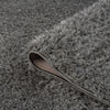 Grey and silver plush shaggy rug with thick polyester fibers and a curved corner showing textured backing.