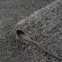 Grey and silver plush shaggy rug with thick polyester fibers and a curved corner showing textured backing.