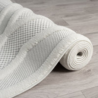 Rolled corner of grey and white rug with textured geometric pattern on light wood floor.