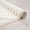 Beige and white geometric diamond patterned rug with textured pile and fringed edges rolled on light wood floor.