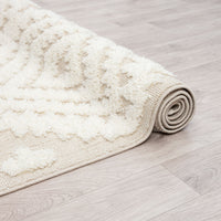 Beige and white geometric diamond patterned rug with textured pile and fringed edges rolled on light wood floor.