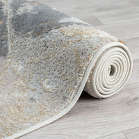 Rolled modern rug with abstract geometric pattern in muted gray, beige, and cream tones on light hardwood floor.