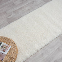 Cream shaggy runner rug on light wood flooring with a woven tray and magazines nearby.