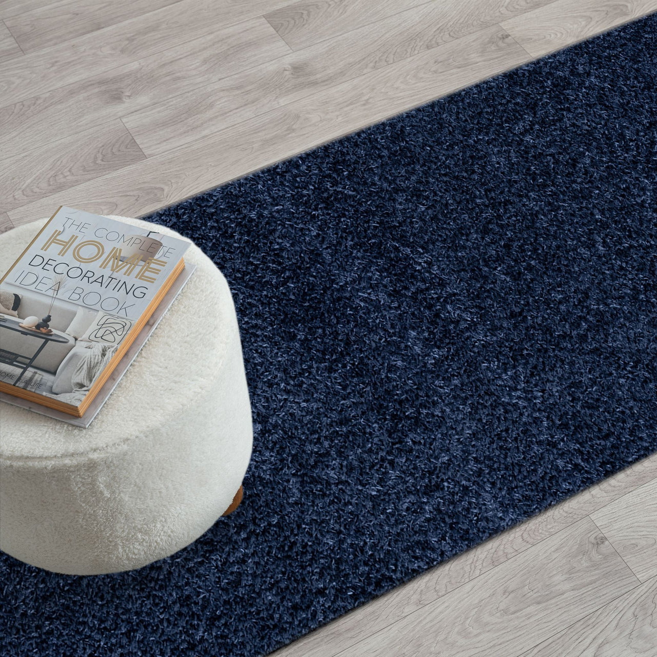 Navy blue modern shaggy runner rug on light wood floor with white ottoman and decor book.