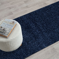 Navy blue modern shaggy runner rug on light wood floor with white ottoman and decor book.