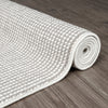Rolled grey and white flatweave runner rug with tight geometric pattern on wooden floor.