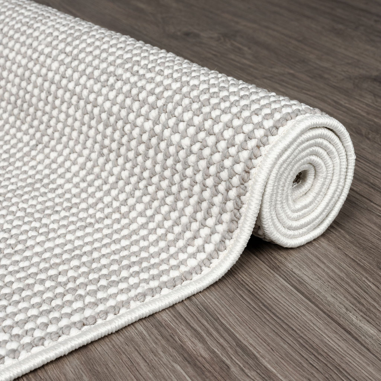 Rolled grey and white flatweave runner rug with tight geometric pattern on wooden floor.