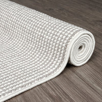 Rolled grey and white flatweave runner rug with tight geometric pattern on wooden floor.