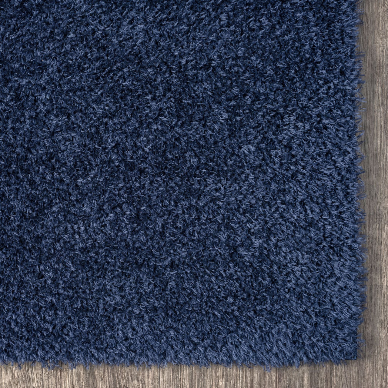 Navy blue shaggy rug with dense, soft polyester fibers on a wooden floor corner.