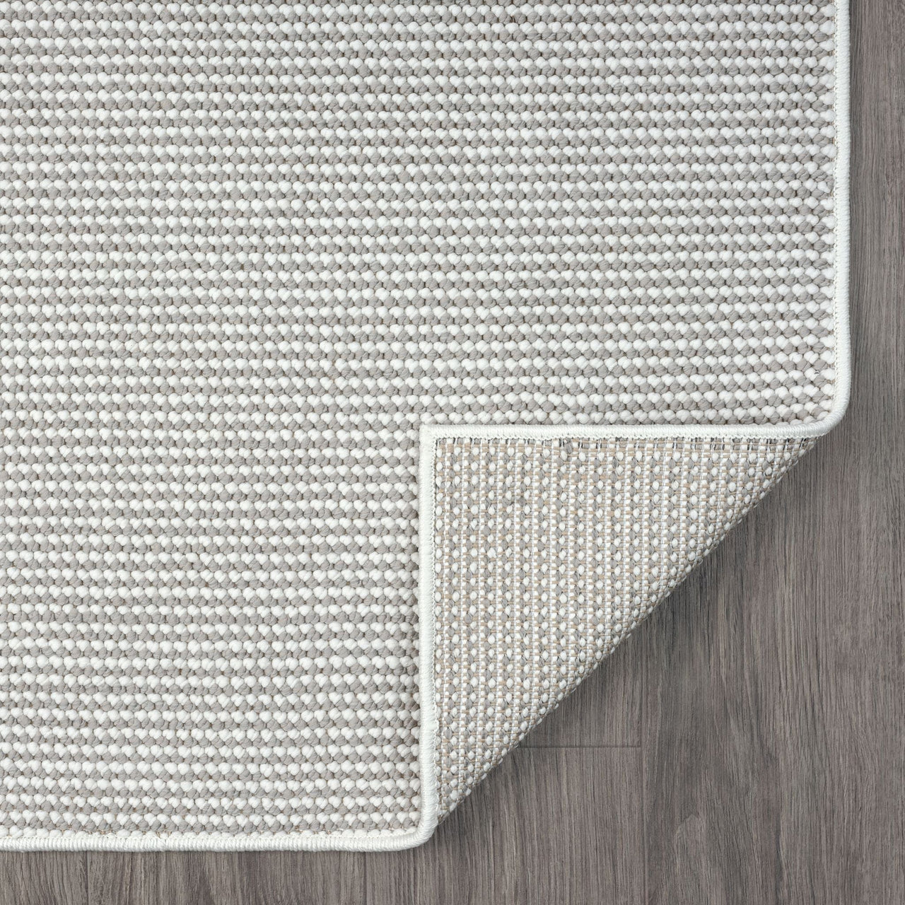 Grey flatweave rug with subtle geometric pattern and neatly finished edges on wood floor.