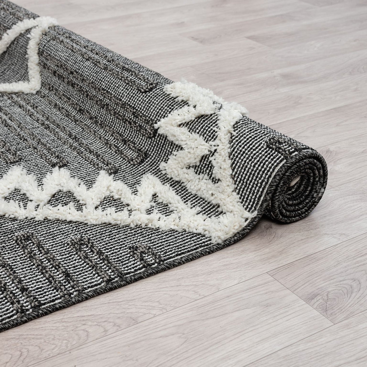 Grey and white geometric patterned runner rug with textured pile and fringed edge on light wood floor.