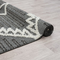 Grey and white geometric patterned runner rug with textured pile and fringed edge on light wood floor.