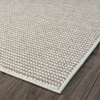 Beige flatweave rug with subtle geometric texture and cream edging on dark wood floor.