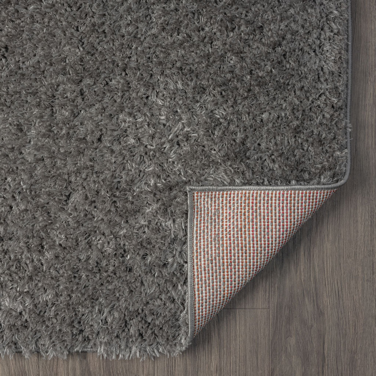 Rectangular grey shaggy rug with dense polyester fibers and a fabric-backed underside shown on wood floor.
