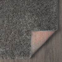 Rectangular grey shaggy rug with dense polyester fibers and a fabric-backed underside shown on wood floor.
