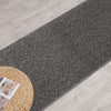 Grey shaggy runner rug with dense pile on light wood flooring next to a woven round mat.