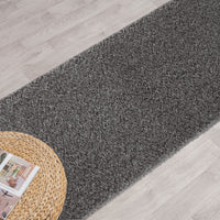 Grey shaggy runner rug with dense pile on light wood flooring next to a woven round mat.