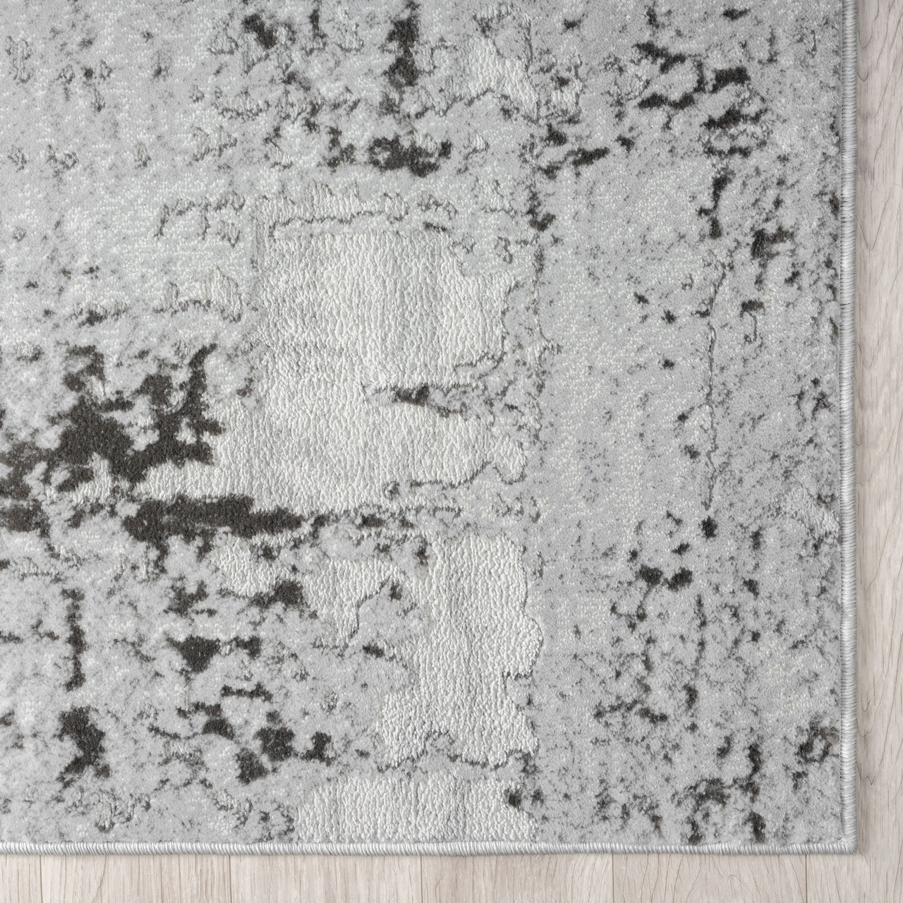 Close-up of a textured gray rug with black accents on a wooden floor.