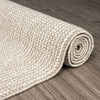 Rolled taupe flatweave rug with textured geometric pattern on wooden floor.