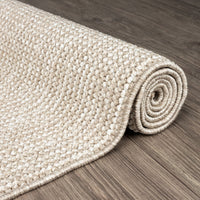 Rolled taupe flatweave rug with textured geometric pattern on wooden floor.