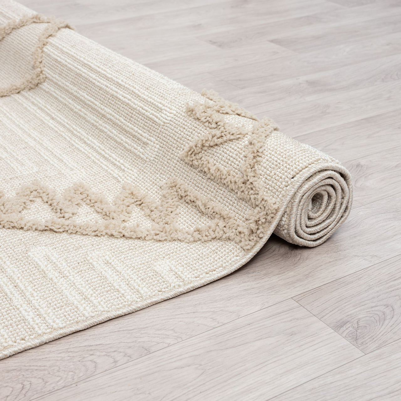 Rolled beige runner rug with textured geometric patterns and fringed edges on light wood floor.